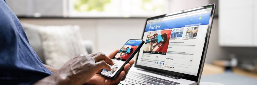 Watching Online News Article On Mobile Phone And Laptop. Electronic Newspaper